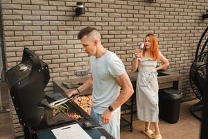 un casado Pareja cocineros A la parrilla carne juntos en su terraza foto