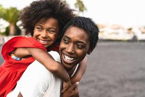 Happy African family having fun on the beach during summer holidays - Afro mother and daughter enjoying vacation days - Parents love and travel lifestyle concept photo