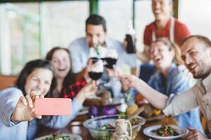 grupo de contento amigos tomando selfie utilizando móvil inteligente teléfono cámara - joven milenario personas teniendo divertido a cena hora - amistad, comida y beber, tecnología y juventud estilo de vida concepto foto