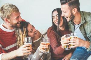 Group of happy friends cheering with beer at home - Millennial Young people having fun drinking and laughing together sitting on sofa - Friendship, entertainment and youth lifestyle holidays photo