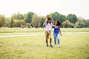 Happy African family walking together in public park - Mother father and baby daughter having fun spending time together outdoor - Happiness, love and parenthood concept photo