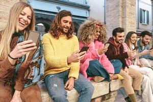 Group friends using mobile smartphone outdoor - Trendy young people having fun with new technology apps for social media phone - Technology and millennial generation culture lifestyle concept photo