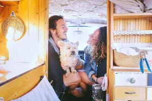 Happy couple having fun in vintage minivan with their dog during a road trip - Young people enjoying time together and laughing in vacation holidays - Relationship and travel youth lifestyle photo