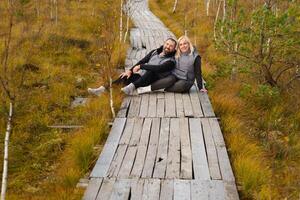 un Pareja se sienta en un de madera camino en un pantano en yelnya, bielorrusia foto