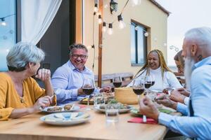 Happy multiracial senior friends having fun dining together on house patio - Elderly lifestyle people and food concept photo