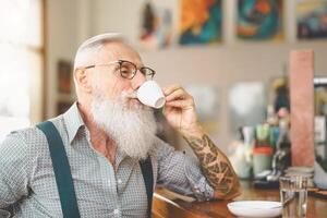 Senior bearded man drinking coffee sitting bar counter - Happy mature male having fun enjoying retired time - Elderly people lifestyle concept photo