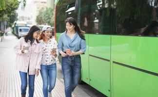 contento asiático muchachas utilizando móvil teléfono inteligente en ciudad - milenario amigos teniendo divertido con nuevo de moda tecnología al aire libre - juventud Generacion estilo de vida y tecnología personas adiccion concepto foto