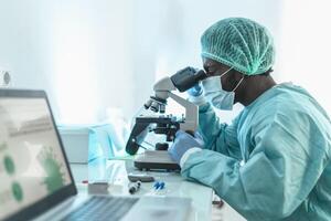 africano médico trabajando en investigación laboratorio examinando microorganismos mediante microscopio - Ciencias y tecnología concepto foto