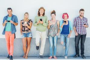 Young people watching on their smart mobile phones leaning on a wall - Generation addicted to new technology - Concept of youth addiction to social network trends photo