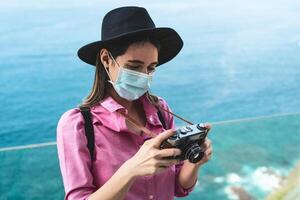 joven viaje mujer fotografiando con antiguo Clásico cámara - contento niña vistiendo cara quirúrgico máscara explorador nuevo turístico destinos - salud cuidado y turismo concepto foto