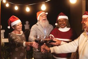 Happy senior friends celebrating Christmas holidays while toasting with red wine glasses on house patio party photo