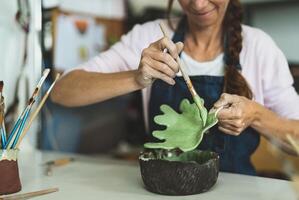 Woman potter painting clay figure in workshop - Artisan work and creative craft concept photo