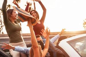 Happy friends having fun on convertible car in road trip - Group young people enjoying vacation together in tropical city - Youth culture lifestyle and travel transportation concept photo