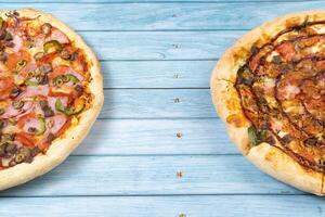 Two different delicious big pizzas on a blue wooden background photo