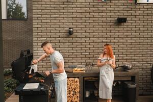 A married couple cooks grilled meat together on their terrace photo