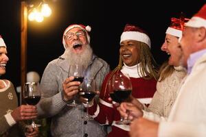 Happy multiracial senior friends celebrating Christmas holidays drinking red wine on house patio party photo