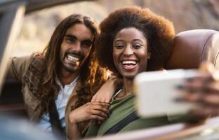 Happy young couple taking selfie with mobile smartphone while doing road trip - Travel people having fun driving in convertible car discovering new places - Relationship and vacation lifestyle concept photo