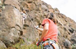 hombre dando asistencia a mujer quien es alpinismo arriba en montaña acantilado - escaladores en acción en alto rock - concepto de extremo deporte estilo de vida personas foto