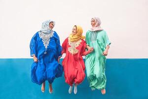 contento musulmán mujer saltando juntos al aire libre - árabe adolescente muchachas teniendo divertido en el ciudad - concepto de gente, disfraz, cultura y religión foto