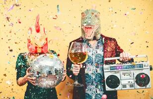 Crazy couple celebrating new year eve wearing chicken and dinosaur t-rex mask - Young trendy people having fun drinking champagne and listening music with vintage boombox - Absurd and holidays concept photo