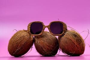 three whole coconuts and wooden glasses on a pink background photo