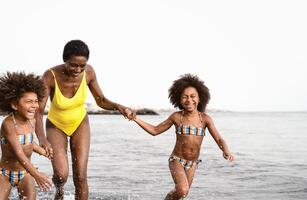 Happy African family running on the beach during summer holidays - Afro American people having fun on vacation time - Parents love and travel lifestyle concept photo