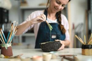 Happy mature woman mixing paint with brush inside ceramic bowl in workshop studio - Artisan work and creative craft concept photo