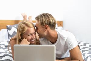 Happy couple lying on bed while using laptop computer - Happy people having funny bed time - Love relationship and technology concept photo