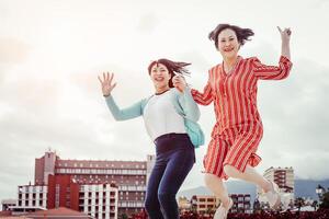 Asian mother and daughter jumping outdoor - Happy family having fun dancing and celebrating outside - Concept of elderly and youth people photo