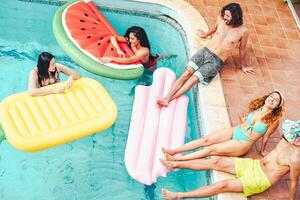 contento amigos teniendo divertido en nadando piscina durante verano tropical vacaciones - joven personas relajante y flotante en aire colchonetas en el piscina recurso - amistad, relajarse, Días festivos y juventud estilo de vida concepto foto