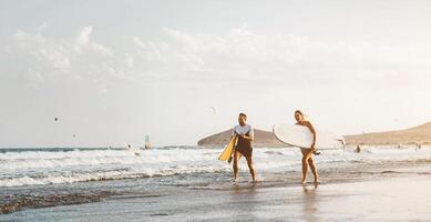 Surfer couple running long sea shore ready to surf on high waves - Sporty friends having fun during surfing day in ocean - Extreme sport health lifestyle people concept photo