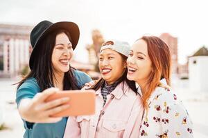 contento asiático muchachas tomando selfie con móvil teléfono inteligente al aire libre - joven de moda adolescente teniendo divertido con nuevo tecnología aplicación - gente, social, amistad, tecnología y juventud estilo de vida concepto foto