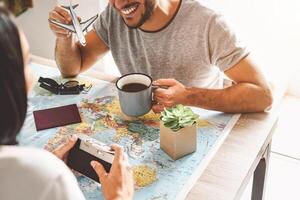 Happy couple planning next travel destination using world map - Young playful people having fun and getting ready for vacation - Relationship and Traveling lifestyle concept photo