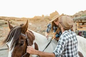 Happy couple of farmers kissing while riding on horse inside corral ranch photo