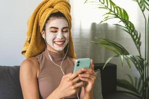 Young woman using mobile smartphone while having skin care spa day at home photo