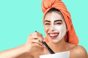 Happy girl applying daily facial cream - Young woman having skin care spa day - Healthy beauty clean treatment and cosmetology products concept - Colored background photo