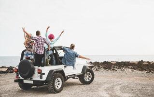 Group of friends driving off road convertible car during roadtrip - Happy travel people having fun in vacation - Friendship, transportation and youth lifestyle holidays concept photo