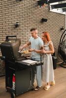 A married couple cooks grilled meat together on their terrace photo