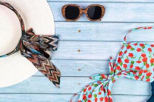 Top view of a straw white hat with glasses and a swimsuit, lying on a blue wooden background.Summer vacation concept photo