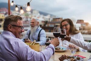 Happy multiracial seniors toasting with red wine glasses together on house patio dinner - Elderly lifestyle people concept photo