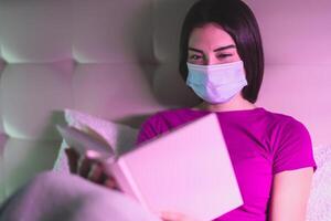 joven mujer vistiendo quirúrgico máscara leyendo libro en cama - salud mental impacto corona virus extensión - Cuidados de salud personas y covid19 confinamiento concepto foto