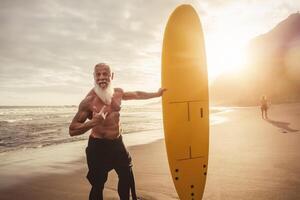 ajuste mayor masculino teniendo divertido surf durante puesta de sol hora - retirado hombre formación con tabla de surf en el playa - mayor sano personas estilo de vida y extremo deporte concepto foto