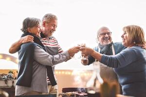 Happy senior friends drinking red wine at barbecue on house patio  - Mature people cheering and dining together at bbq party - Food and elderly friendship lifestyle concept photo