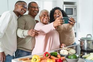 Happy Latin family having fun taking selfie with mobile smartphone while preparing healthy lunch in modern kitchen at home - Food and parents unity concept photo