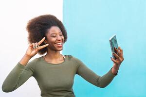 afro americano niña tomando selfie con móvil teléfono inteligente al aire libre - contento hombre de influencia teniendo divertido con nuevo tecnología aplicaciones - personas tecnología adiccion y social medios de comunicación estilo de vida concepto - azul antecedentes foto