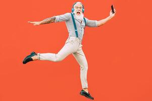 Senior crazy man jumping while listening music outdoor - Hipster male having fun dancing and celebrating life outside - Happiness, technology and elderly lifestyle people concept photo