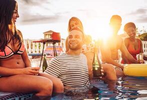 Group of happy friends making a pool party drinking champagne at sunset on vacation - Young people laughing and having fun with sparkling wine in luxury tropical resort - Youth lifestyle concept photo