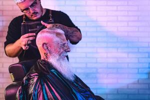 masculino peluquero corte pelo a hipster mayor cliente - lado ver de joven estilista trabajando en barbería - Corte de pelo profesión concepto foto