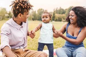 Happy African family having fun together in public park - Black mother father and baby daughter enjoying lovely time outdoor - Happiness, love and parenthood lifestyle concept photo