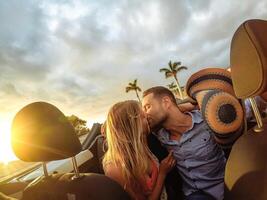 de moda joven Pareja teniendo un oferta momento en convertible coche durante su la carretera viaje - contento romántico recién casado fecha besos en cabriolé auto - amar, relación y juventud romance Días festivos estilo de vida foto